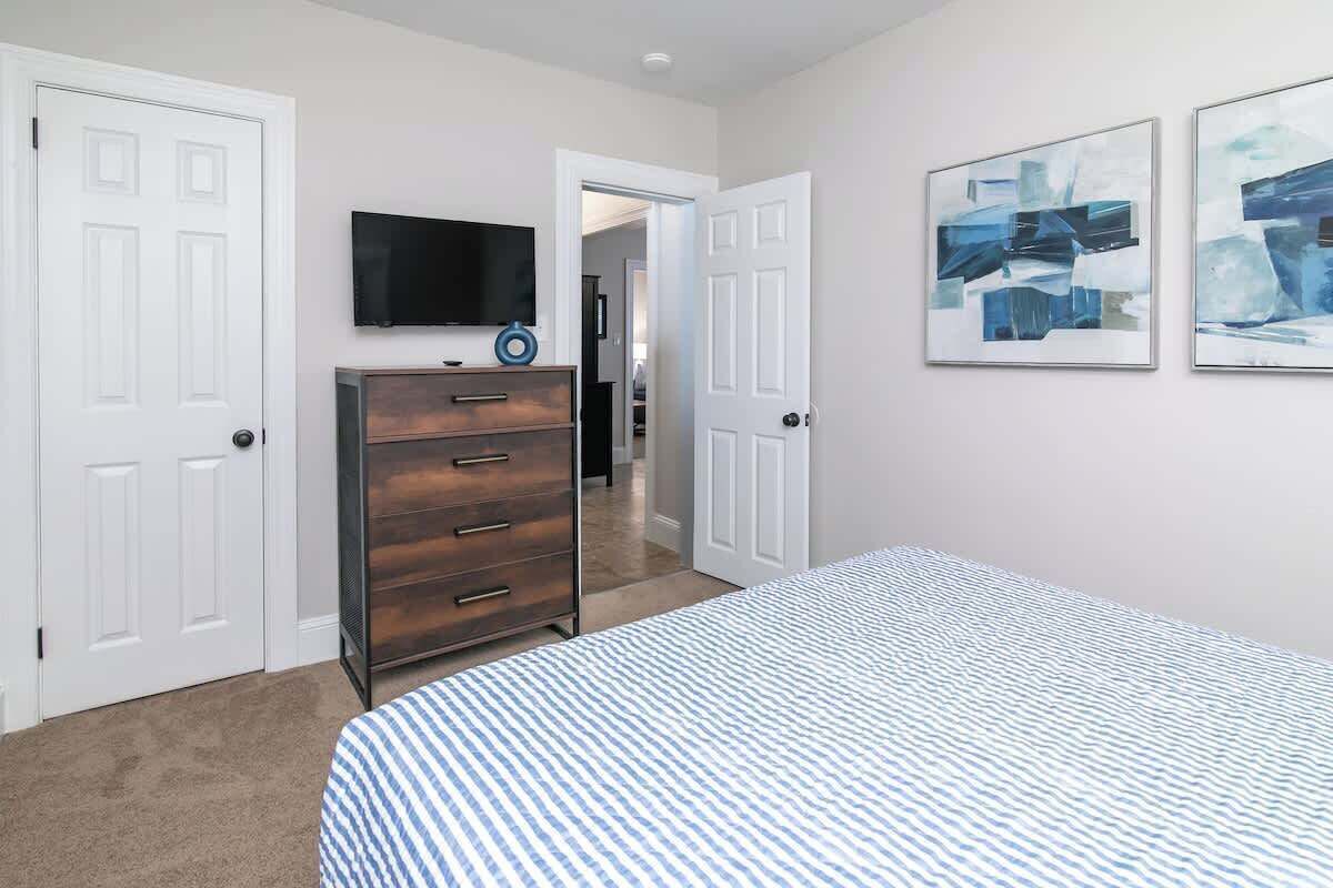 A bedroom with a bed, dresser, TV, and abstract art on the wall.