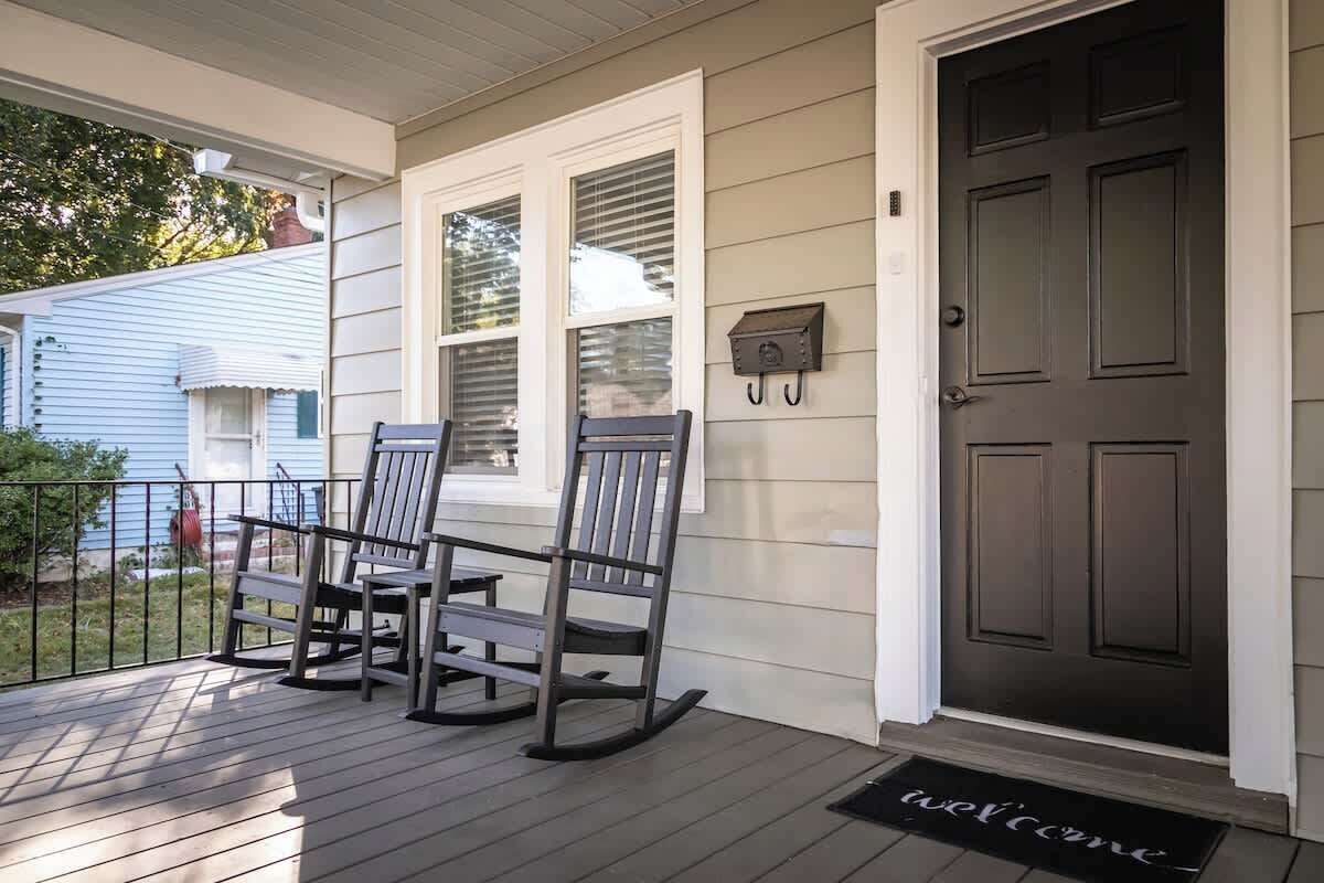 A porch with two rocking chairs, a dark door, and a welcome mat.