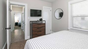 Une chambre à coucher avec un lit, une commode, une télévision et un miroir.