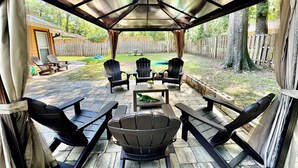 Un patio couvert avec des sièges d’extérieur et une piscine en arrière-plan.