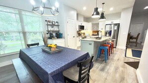 Une cuisine moderne avec des meubles blancs, un îlot central et un coin repas agrémenté d’une nappe bleue.