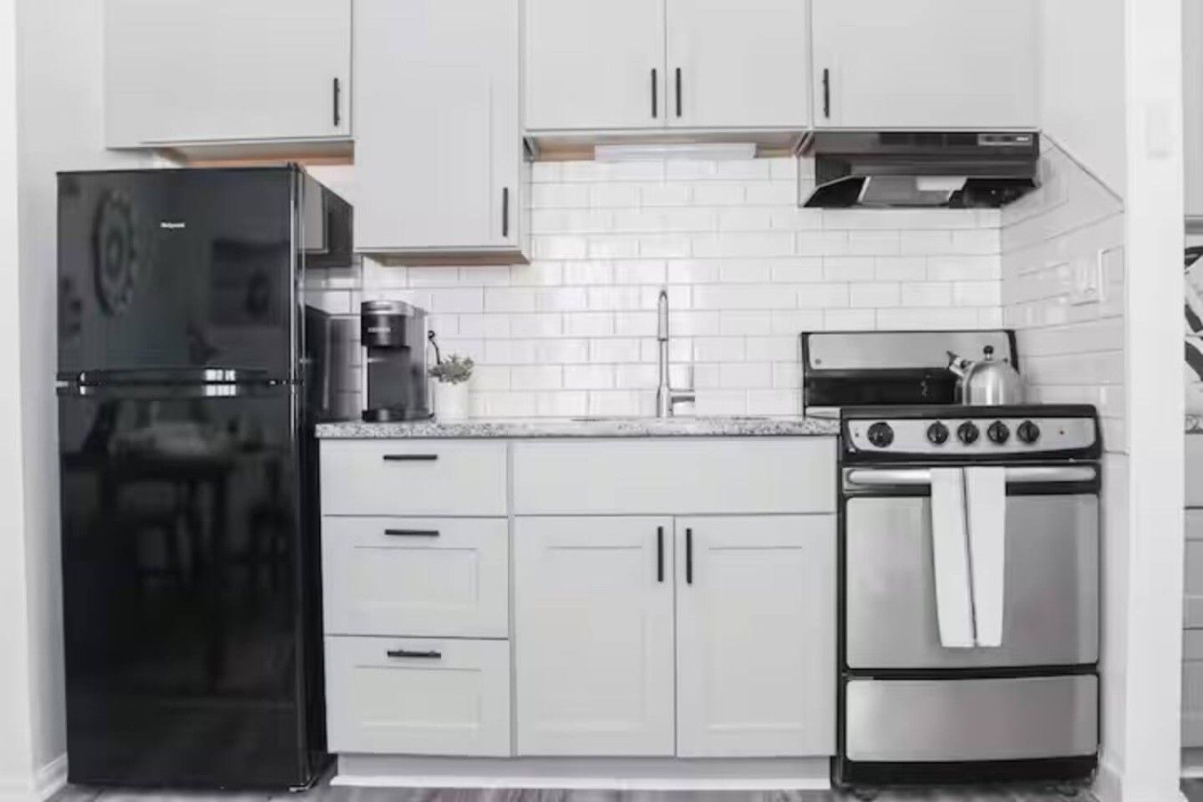 Una cocina con armarios blancos, un refrigerador negro, una cafetera y una estufa.