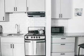 A kitchen with white cabinets, a stainless steel stove, a microwave, and a tiled backsplash.