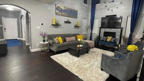 Uma sala de estar com um sofá cinzento, uma mesa de centro, um tapete branco e uma lareira.