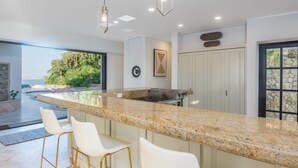 Una cocina moderna con encimera de granito, taburetes de bar blancos e iluminación colgante.