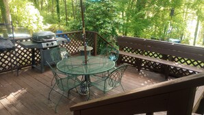 A wooden deck with a metal table and chairs, a barbecue grill, and a wooden bench. - Local Events House on Lake near HPU, High Point Markets, NC Hospitals  (High Point)