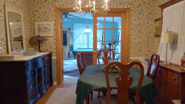 A dining room with a table set for four, surrounded by wooden chairs. A chandelier hangs above the table, and there is a wooden cabinet to the left. - Local Events House on Lake near HPU, High Point Markets, NC Hospitals  (High Point)