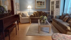 A living room with a piano, two sofas, a coffee table, and a cabinet. - Local Events House on Lake near HPU, High Point Markets, NC Hospitals  (High Point)