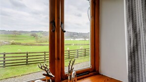 A room with large windows offering a view of a green field with sheep. - Shepherds Cottage (Ambleside)