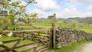 A rural landscape with a wooden gate and stone wall, leading to a grassy field. - Shepherds Cottage (Ambleside)