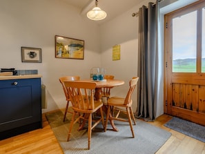 A dining area with a wooden table and chairs, a painting on the wall, and a view of the outdoors through a door. - Shepherds Cottage (Ambleside)