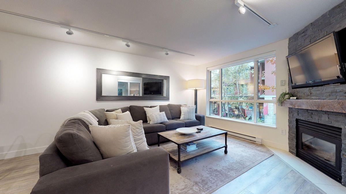 Un salon moderne avec un canapé, une table basse, une cheminée et de grandes fenêtres.