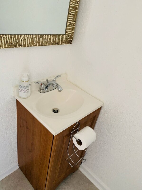 A bathroom with a white sink, a mirror with a gold frame, and a wooden cabinet. - Close to Store and Airport (Kenner)