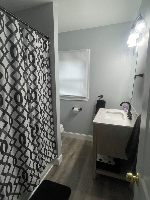 A bathroom with a shower curtain, toilet, sink, and a window with blinds.