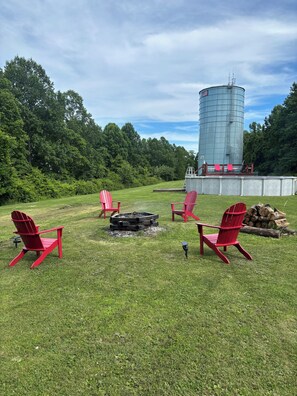 A grassy outdoor area with red chairs, a fire pit, and a large cylindrical water tank in the background.