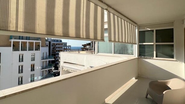 Un balcón moderno con vistas a un paisaje urbano, que incluye un sofá y una mesita.