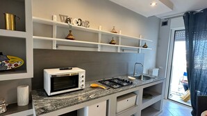 Una cocina moderna con microondas integrado, cocina a gas y un lavabo. Hay armarios y estantes blancos con objetos decorativos.