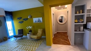 Una sala de estar moderna con una pared de acento amarilla, un tapete estampado y una zona de estar con una silla y una mesita.