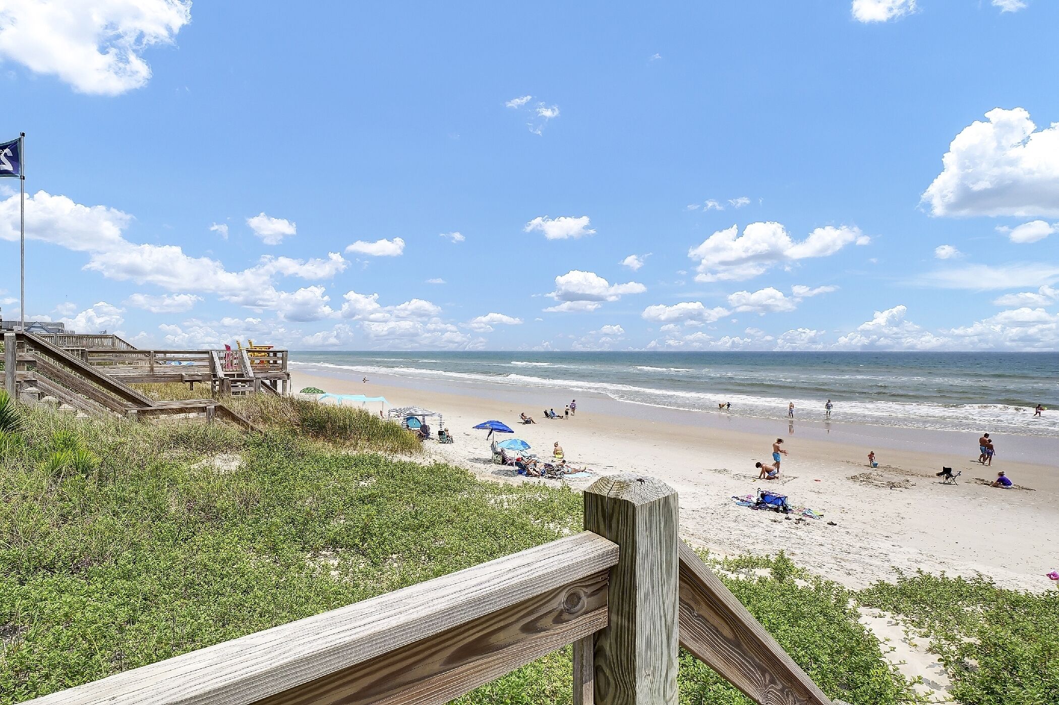 Une plage avec une promenade en bois, des parasols et des gens qui se détendent.