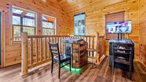 Interior de una cabaña de madera con barra, dos sillas, un televisor y una barandilla de madera.