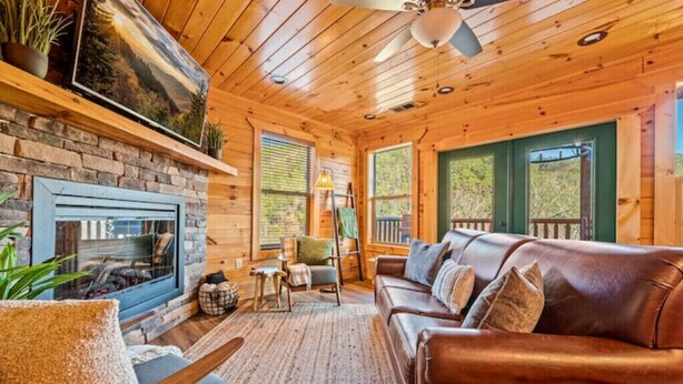 Interior acogedor de una cabaña con chimenea de piedra, sofá de cuero y techo de madera.