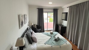 A modern hotel room with a large bed, a desk, a chair, a TV, and a window with curtains. - Retiro Termal no Centro do Vulcão das Furnas (Furnas)