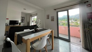 A modern living room with a dining area, a TV, and a balcony with a view. - Retiro Termal no Centro do Vulcão das Furnas (Furnas)