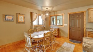 A dining area with a wooden table and chairs, a chandelier, and a door with a mirror. - Cozy Lead Cabin w/ Deck < 1 Mi to Ski Slopes! (Lead)