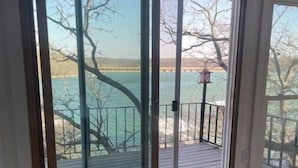 A room with a large sliding glass door leading to a deck with a view of a lake and trees. - Lakehouse front property swim off pier!  (Cisco)