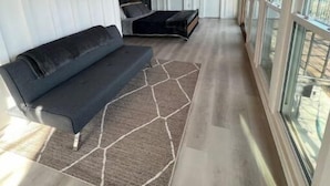 A modern interior with a wooden ceiling, a black sofa, a patterned rug, and large windows. - Lakehouse front property swim off pier!  (Cisco)