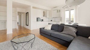 A modern living room with a grey sofa, a glass coffee table, and a kitchen area in the background. - GuestHost - Bright, brand new Apartment- Milano Centrale (Milano)