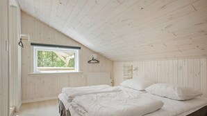 Ein Schlafzimmer mit schrägen Wänden, einem Fenster mit Blick auf Grünflächen, einem Bett mit weißer Bettwäsche und einer Holzwand.