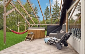 Eine Holzterrasse mit Whirlpool, Liegestühlen und einer Hängematte.