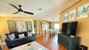 Un salon avec un canapé bleu foncé, une table basse, un téléviseur posé sur un meuble et un ventilateur de plafond.