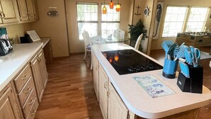 Une cuisine spacieuse avec des meubles en bois, un grand îlot central doté d’une plaque de cuisson et un éclairage suspendu.