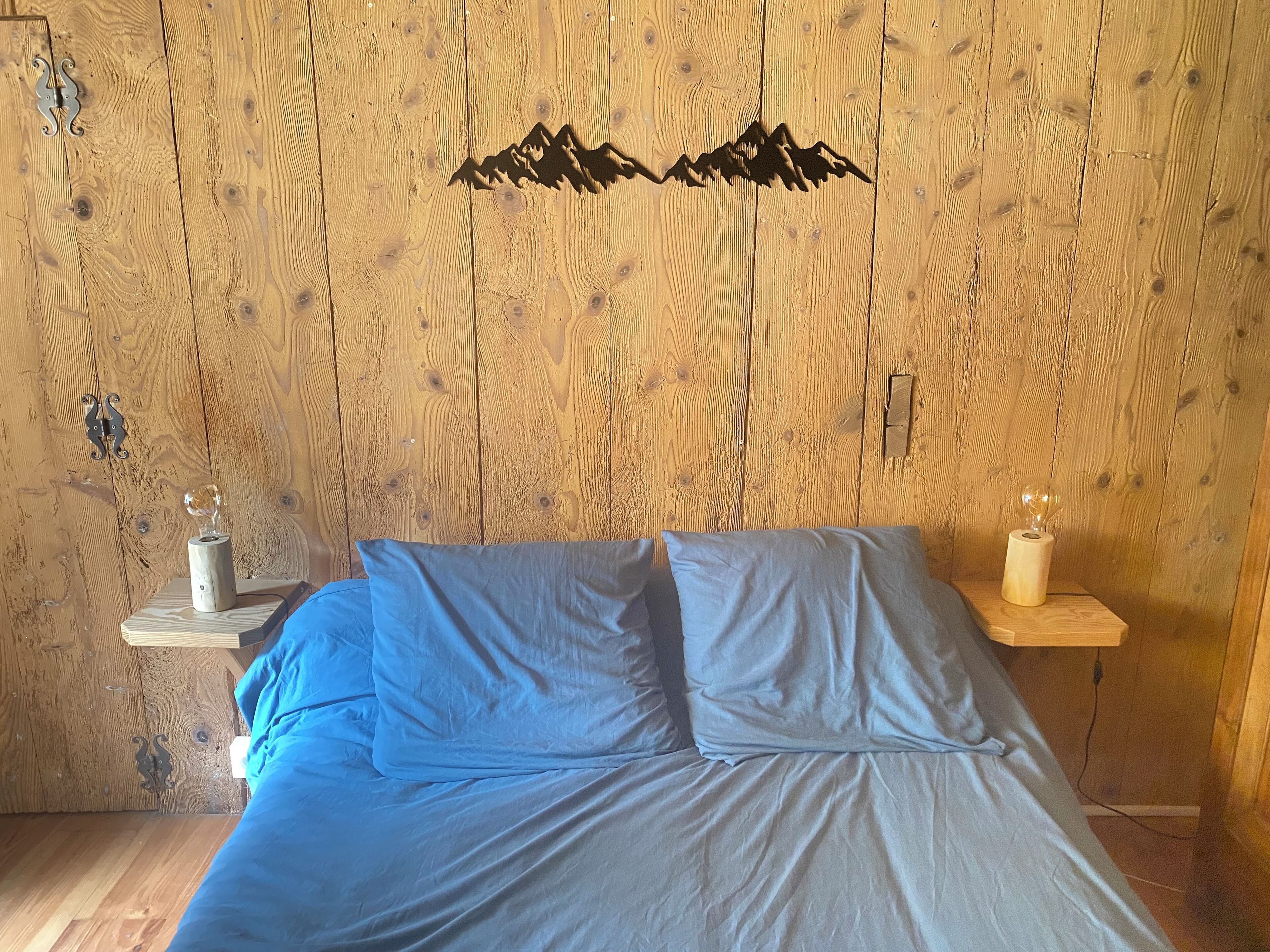 A bedroom with a wooden wall, a bed with blue bedding, and two bedside tables with decorative items.