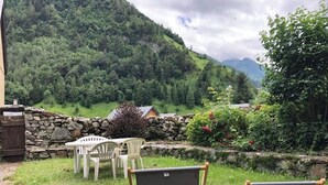 A garden with a stone wall, two folding chairs, and a white table.