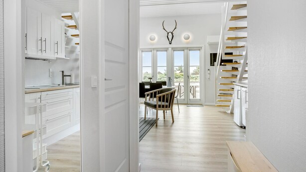 Une cuisine moderne avec des meubles blancs, un coin repas doté d’une table et de chaises noires, et un escalier avec des marches en bois.