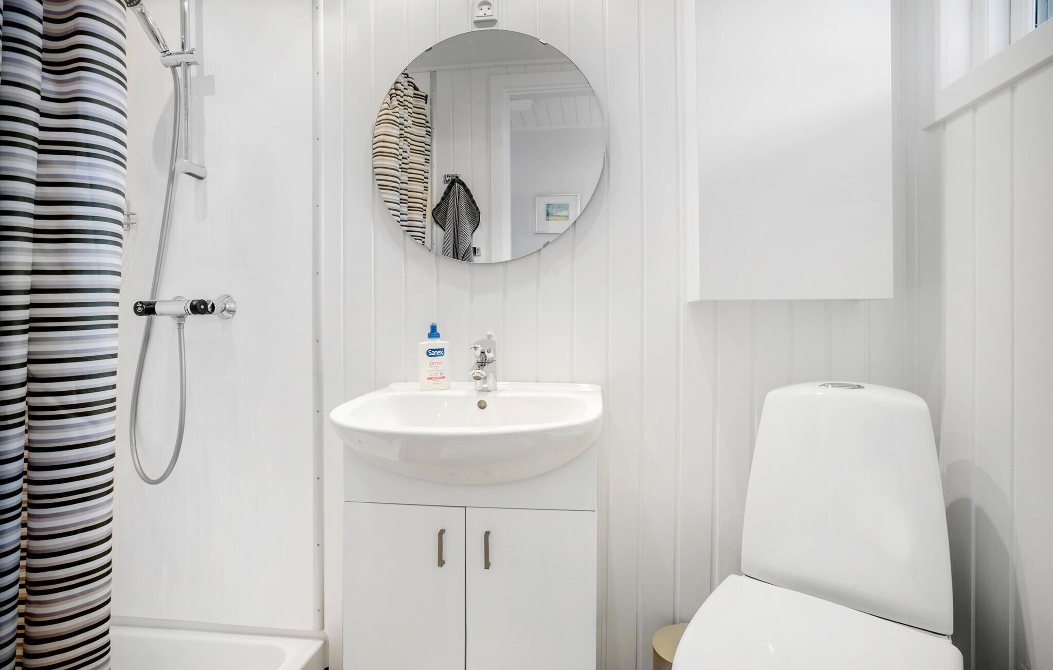 Een badkamer met een witte wastafel, een spiegel, een douche en een toilet.