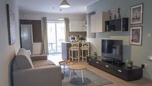 A modern living room with a sofa, TV, and a small dining area with chairs and a table. - Convenient Central 3BR Apt Near Bus Terminus (St. Paul's Bay)