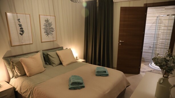 A neatly made bed with two folded towels, a bedside table with a lamp, and two framed botanical prints on the wall. - Convenient Central 3BR Apt Near Bus Terminus (St. Paul's Bay)