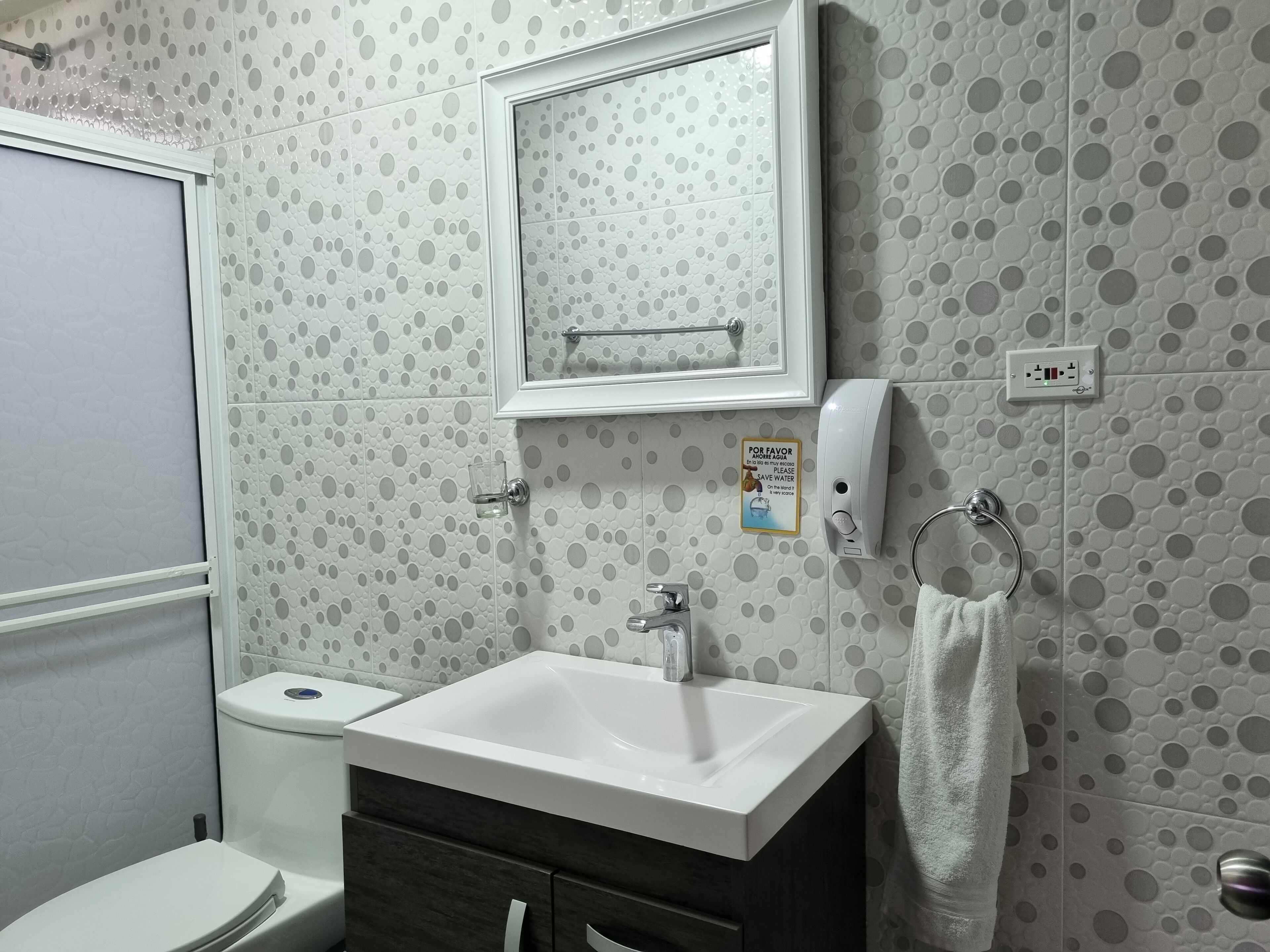 A bathroom with a toilet, sink, and mirror. There is a towel rack and a soap dispenser.