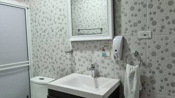 Une salle de bain équipée de toilettes, d’un lavabo et d’un miroir. On y trouve également un porte-serviettes et un distributeur de savon.