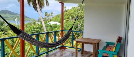 A hammock on a balcony with a view of a lake and mountains.