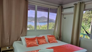 Hotelkamer met een bed, nachtkastje en raam met uitzicht op water en heuvels.