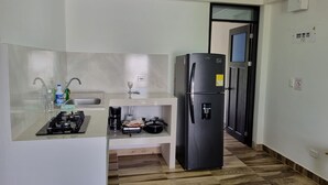 Een kleine keuken met een gasfornuis, spoelbak en een zwarte koelkast.