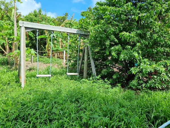 A wooden swing set in a lush garden with dense foliage and trees in the background.
