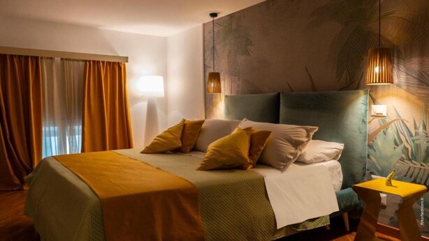 A hotel room with a large bed, a nightstand, a lamp, and a wall with a tropical mural. - Two rooms chiaia 37  (Napoli)