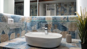 A bathroom with a round sink, a glass shelf, and patterned tiles. - Two rooms chiaia 37  (Napoli)