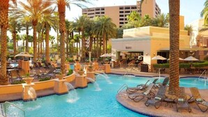 A pool area with lounge chairs and palm trees, surrounded by a building with a sign that reads "WAVES". - Las Vegas | Pool & Strip Access | Urban Comfort Stay (Las Vegas)